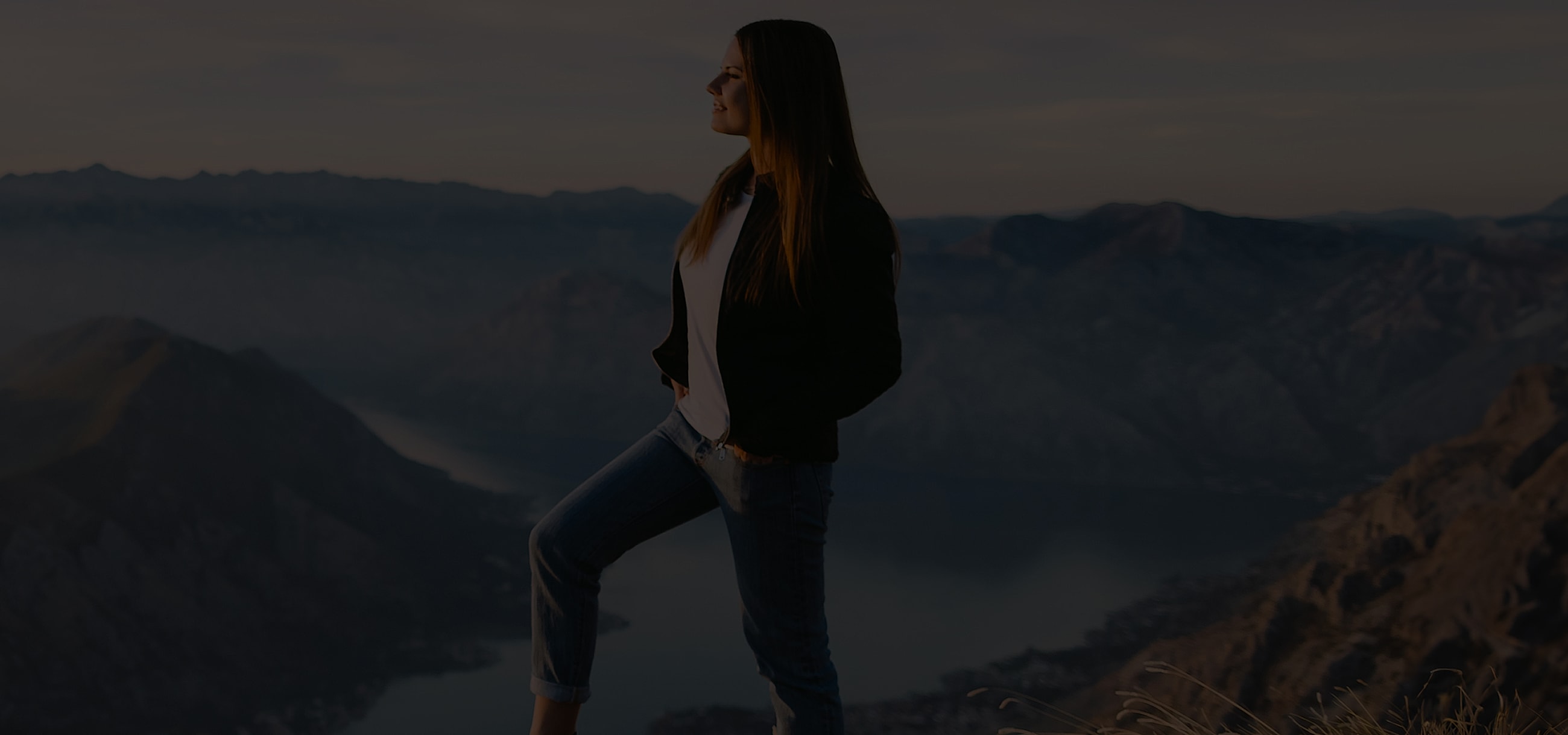 Woman standing on a mountain peak at sunset.