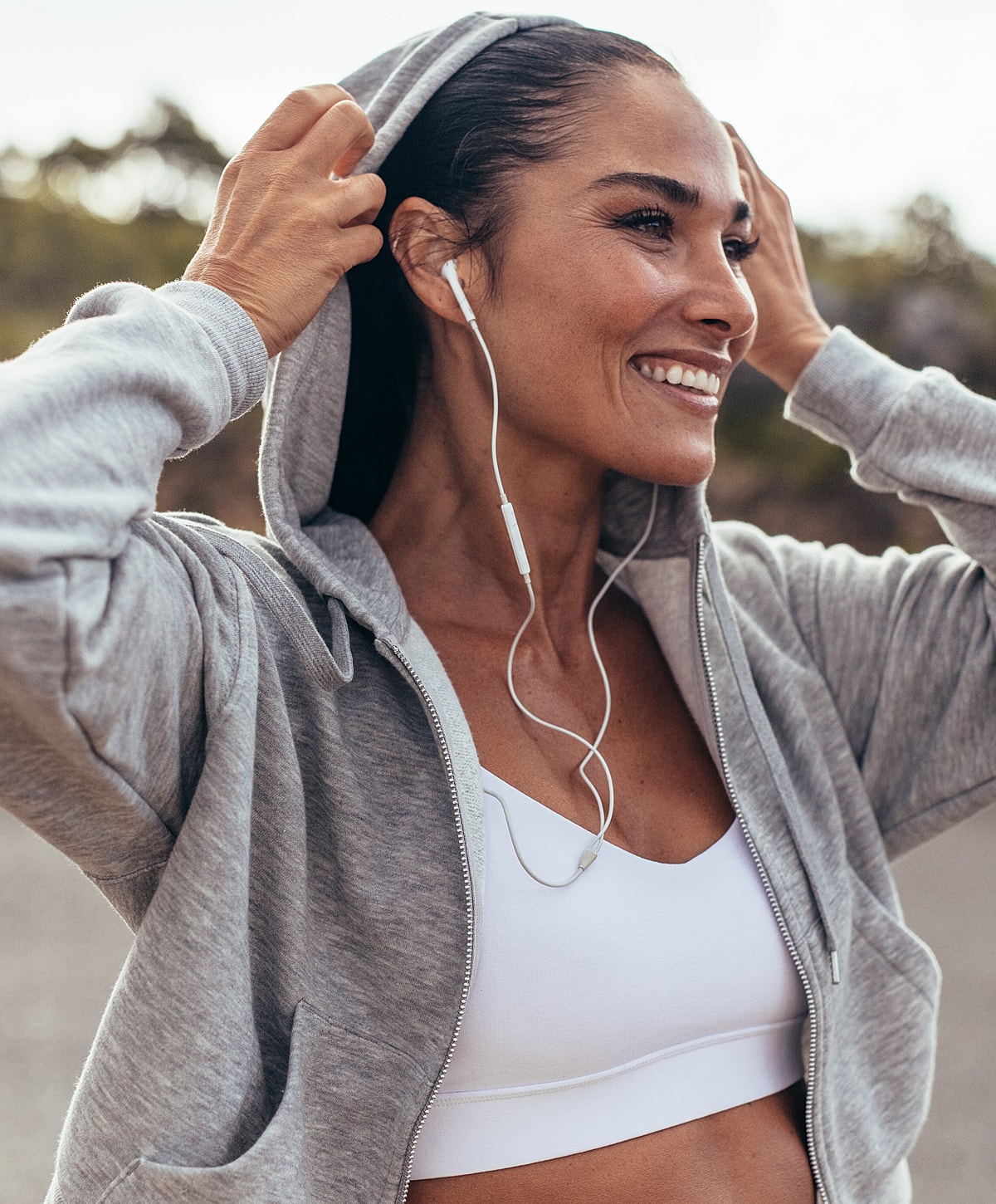 Smiling woman in hoodie wearing earphones outdoors.
