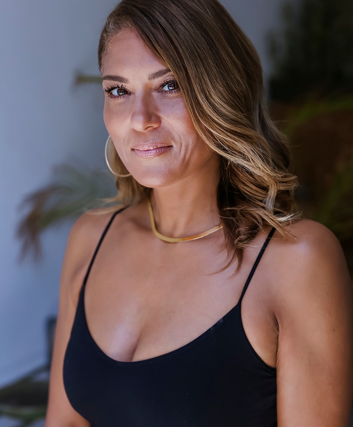 Smiling woman in black outfit with gold necklace.