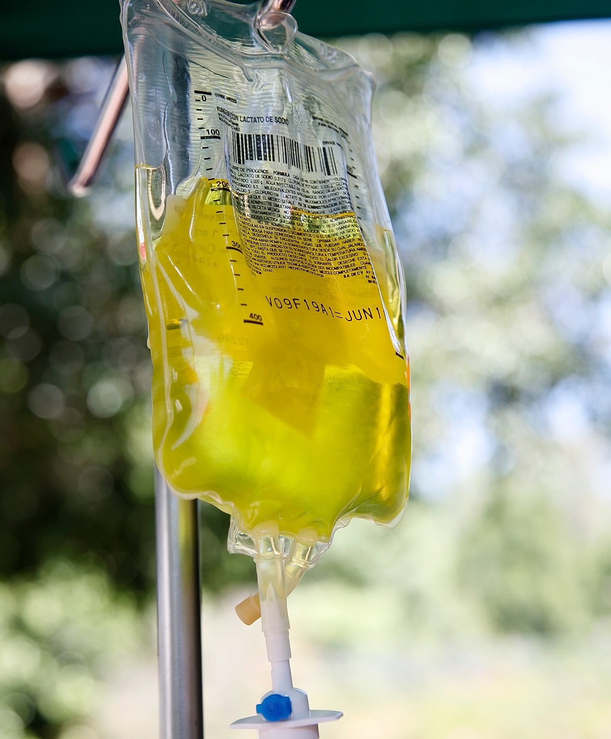 IV bag with yellow fluid hanging outdoors.