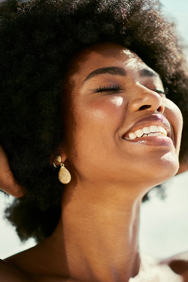 Smiling woman with curly hair in sunlight.