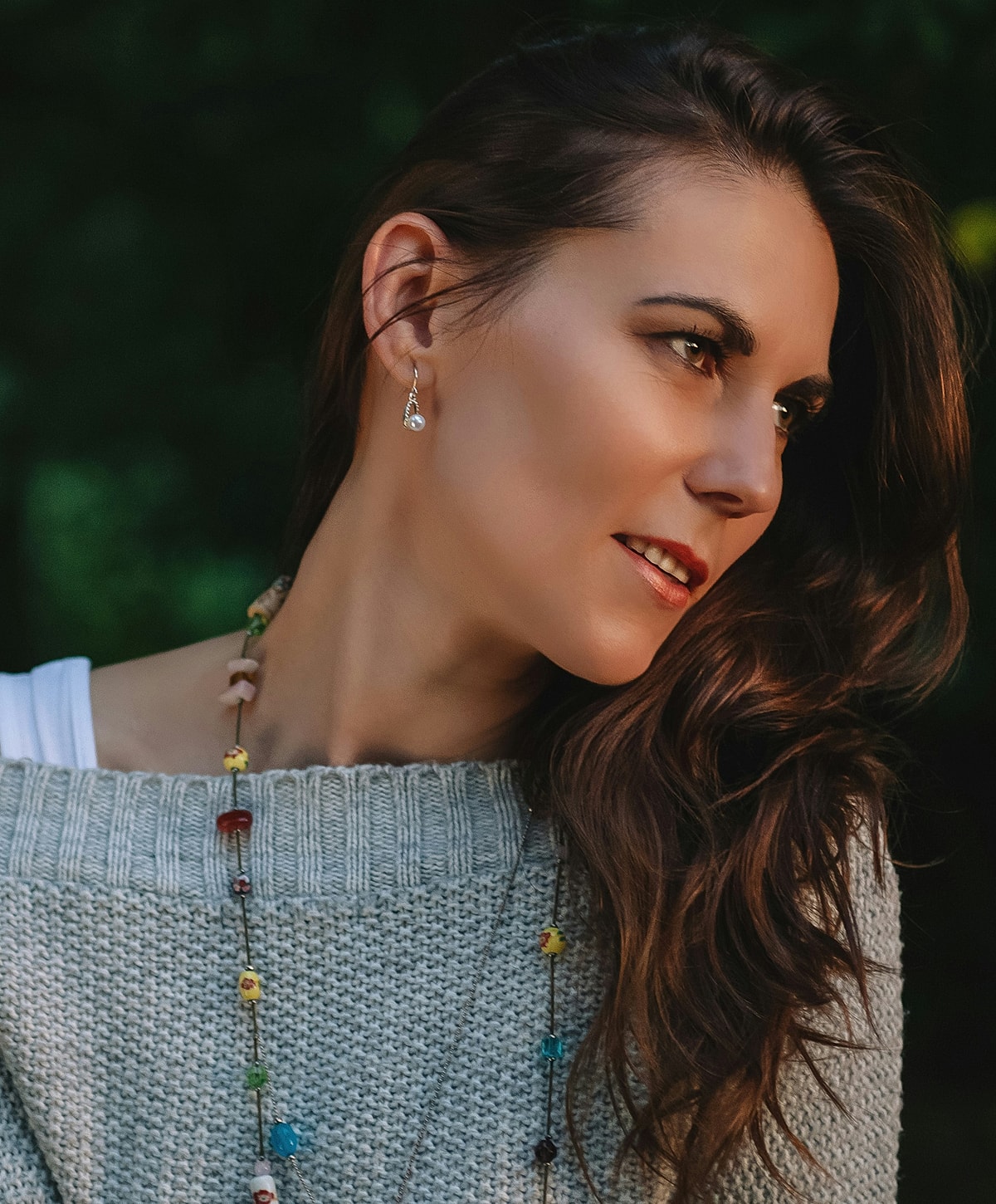 Woman in cozy sweater with necklace, outdoor setting.