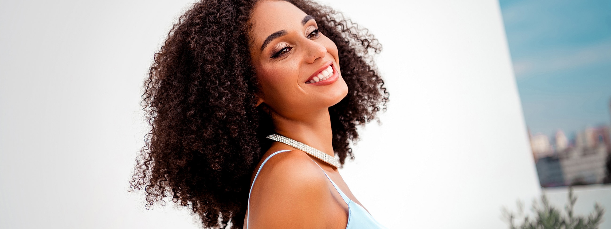 Smiling woman with curly hair and necklace.