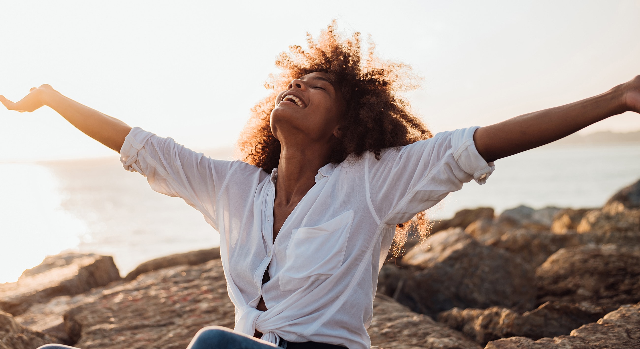Woman enjoying nature on rocky beach at sunset.