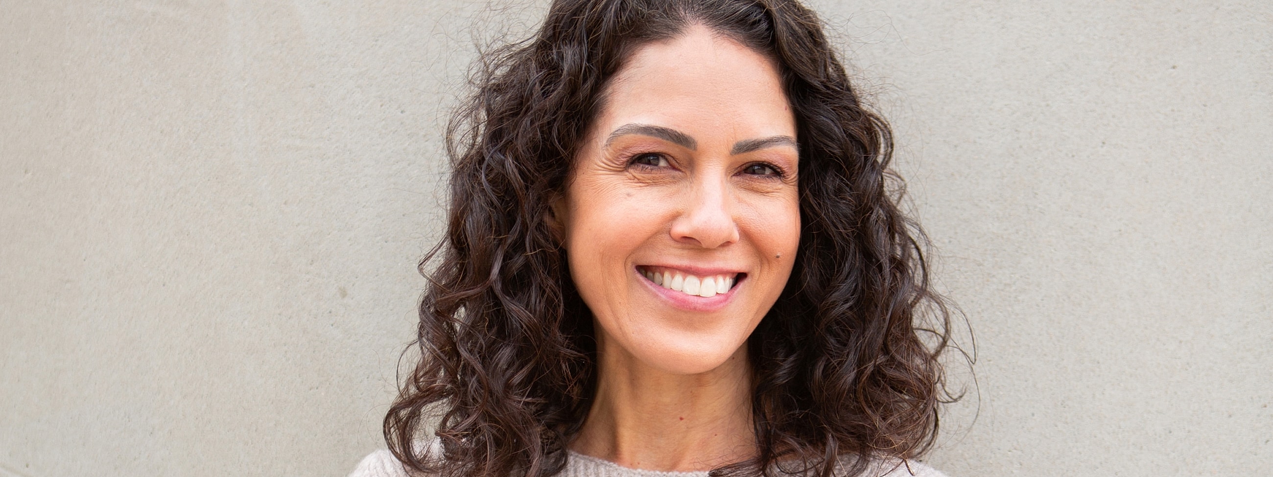 Smiling woman with curly hair against wall.
